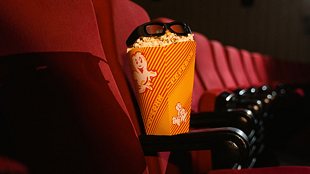 Eine Türe Popcorn mit einer Brille oben drauf steht auf der Armlehne eines Kinosessels
