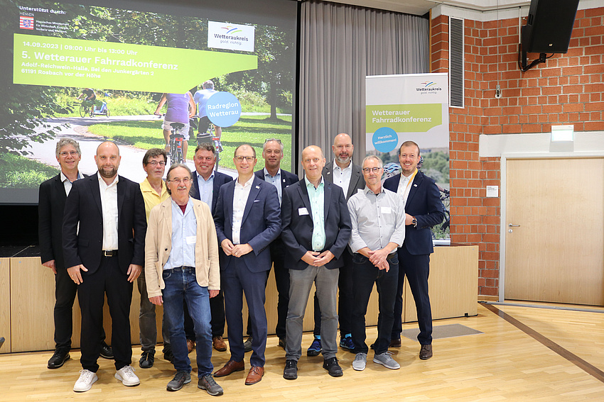 Die uahlreichen Personen stehen vor der Leinwand mit der Werbung für die Radkonferenz.