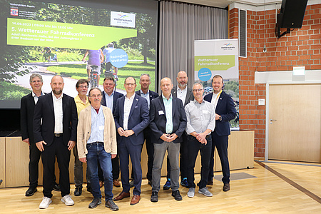 Die uahlreichen Personen stehen vor der Leinwand mit der Werbung für die Radkonferenz.