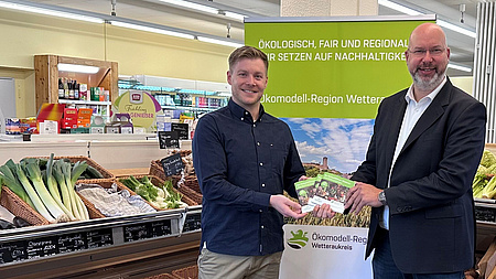 Matthias Walther und Yannik Rudolf halten den Einkaufsführer in der Hand. Im Hintergrund ist ein Roll-Up zu sehen.