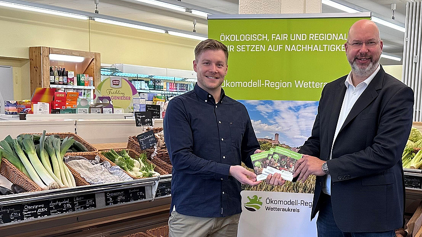 Matthias Walther und Yannik Rudolf halten den Einkaufsführer in der Hand. Im Hintergrund ist ein Roll-Up zu sehen.