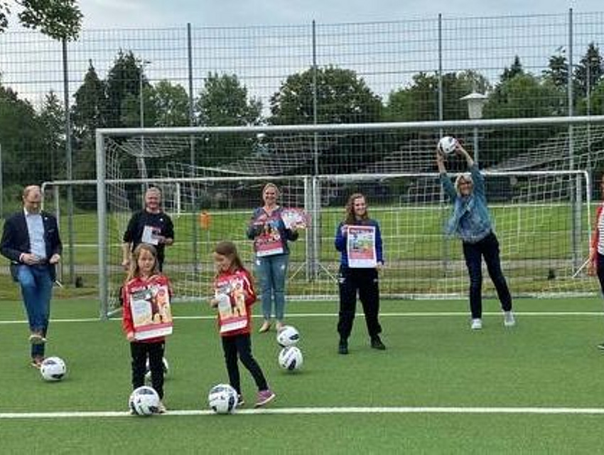 Vor einem Fußballtor auf grünem Rasen präsentieren sich Organisatorinnen, Unterstützer und Spielerinnen des Mädchenfußballtages.