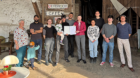 Eine Gruppe von Leuten in einer Scheune. Zwei von ihnen halten ein Dokument in der Hand.
