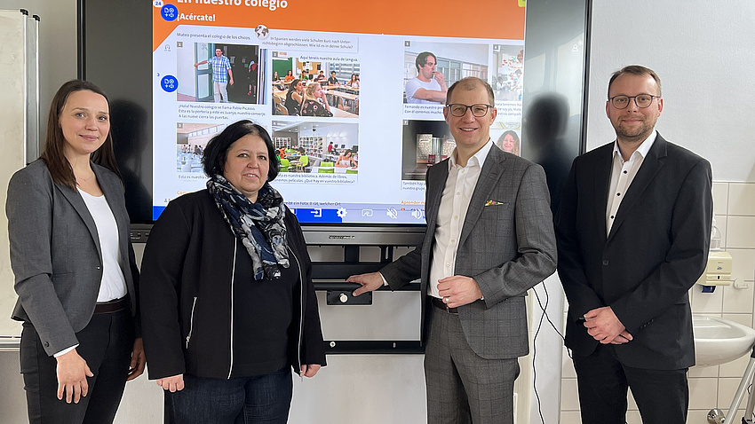 Lehrerin Katharina Bernedo Fernández zeigt Landrat Jan Weckler, DigitalPakt-Projektleiter Andreas Haas und der stellvertretenden Schulleiterin Katrin Zimpel die neuen digitalen Möglichkeiten im Klassenraum. Zwei Frauen und zwei Männer stehen vor einer elektronischen Tafel.