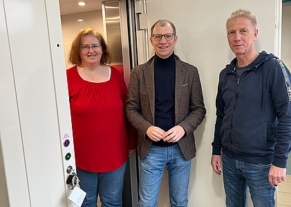 Zwei Männer und eine Frau stehen in einer offenen Tür.