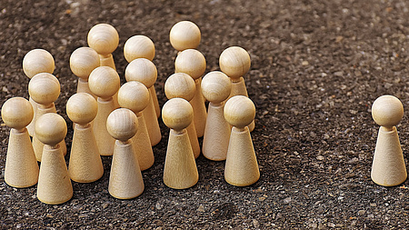 Eine kleine Spielfigur steht alleine einer Gruppe von Spielfiguren gegenüber.