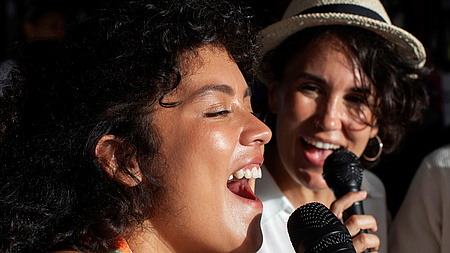 Das Bild zeigt zwei Frauen beim Singen mit einem Mikrofon.