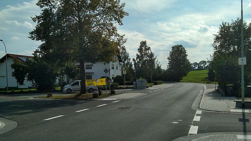 Eine Straße, die am Horizont eine Linkskurve macht. Links sind Häuser. Auf der Straße ist kein Auto unterwegs.