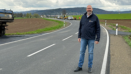 Ein Mann steht auf einer neu geteerten Straße. Im Hintergrund sind Baufahrzeuge zu sehen.