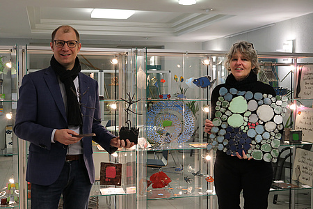 Landrat Jan Weckler und Ulrike Obenauer halten Ausstellungstücke in den Händen. Im Hintergrund Vitrinen mit weiteren Exponaten