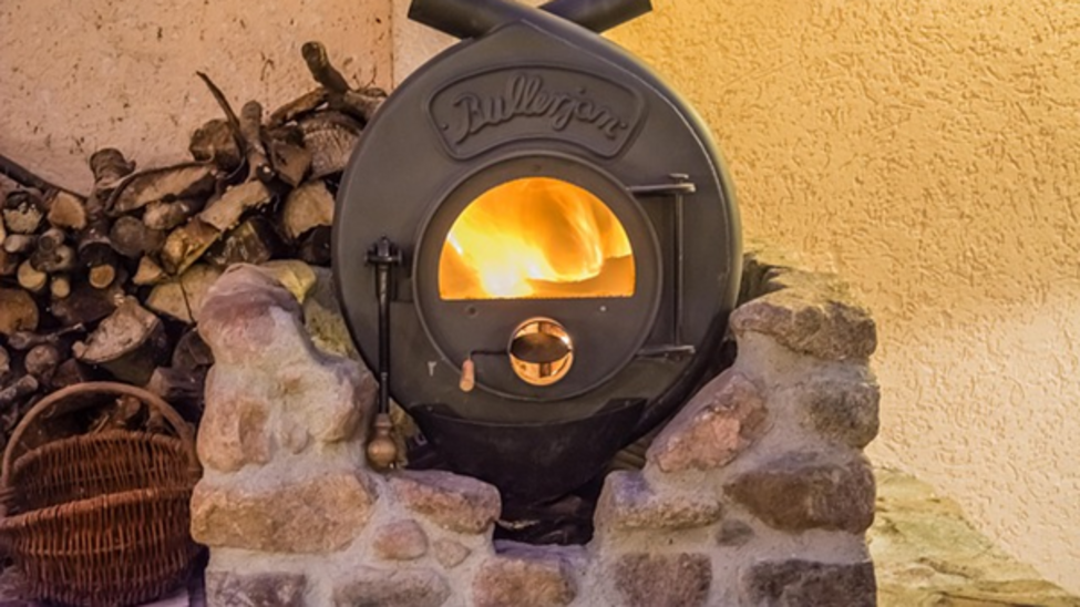 Runder Gusseisener Ofen in einem Steinbett, darin Flammen