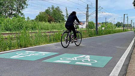 Zu sehen ist ein Radweg, auf dem eine Radfahrerin unterwegs ist.