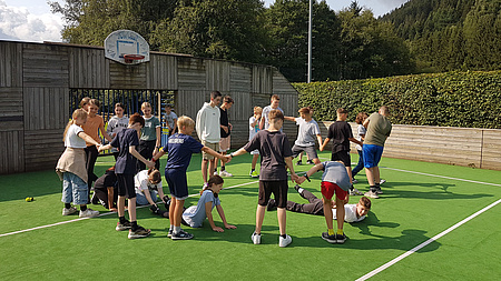 Eine Gruppe Jugendlicher, die auf einem Sportplatz im Kreis stehen.