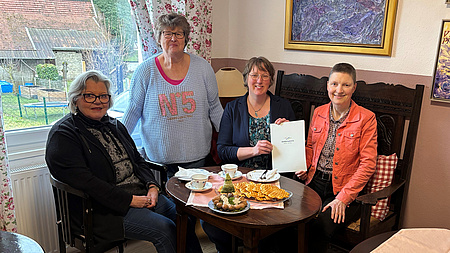 Vier Frauen an einem Tisch. Sie halten den Förderbescheid in die Kamera.
