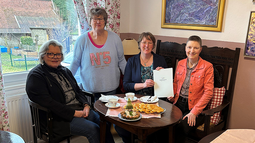 Vier Frauen an einem Tisch. Sie halten den Förderbescheid in die Kamera.