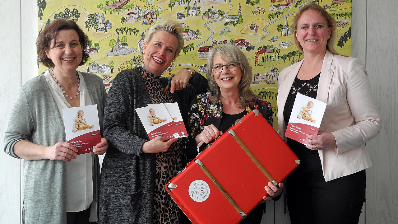 Erste Kreisbeigeordnete Stephanie Becker-Bösch, Fachbereichsleitung Simone Schestakoff, Fachstellenleitung Andrea Rosenberger und Netzwerkkoordinatorin Romy Nickel präsentieren den roten Koffer des Netzwerks Frühe Hilfen für einen Presseartikel.