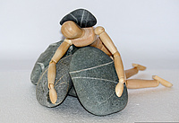 Holzfigur liegt auf Steinen und wird zudem von einem Stein niedergedrückt.