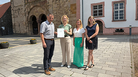 Vier Personen stehen bei der Bescheidübergabe nebeneinander.