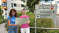 Zwei Frauen stehen vor dem Gebäude des Caritaszentrum St. Bardo bei der Übergabe eines Förderbscheids.