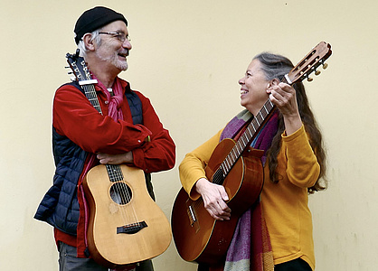 Ein Mann und eine Frau mit Gitarren in der Hand strahlen sich an