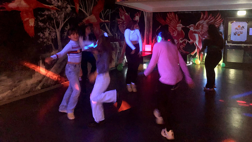 Ein Gruppe von Mädchen tanzt in einem abgedunkelten Raum.