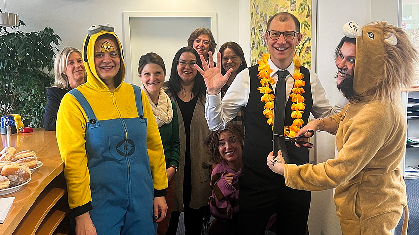 Ein Mann und mehrere Frauen, einige von ihnen im Faschuingskostüm. Eine der Frauen sachneidet dem Mann die Krawatte ab.