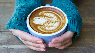 behandschuhte Hände umschließen eine Tasse mit Kaffee 