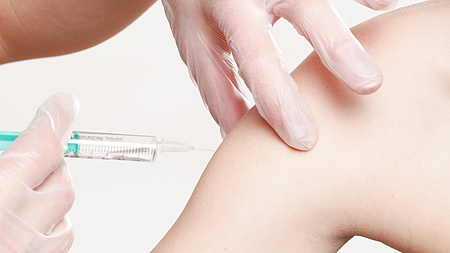 Nahaufnahme eines Impfvorgangs. Eine Person mit Handschuhen verabreicht einem Patienten eine Impfung.
