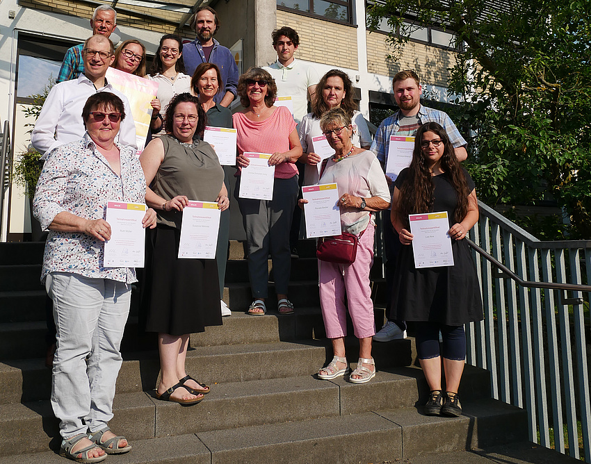 Mehrere Personen stehen auf einer Treppe. Alle haben ein Schriftstück in der Hand.