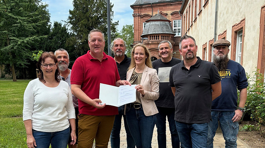 Acht Männer und Frauen stehen vor einem historischen Gebäude.