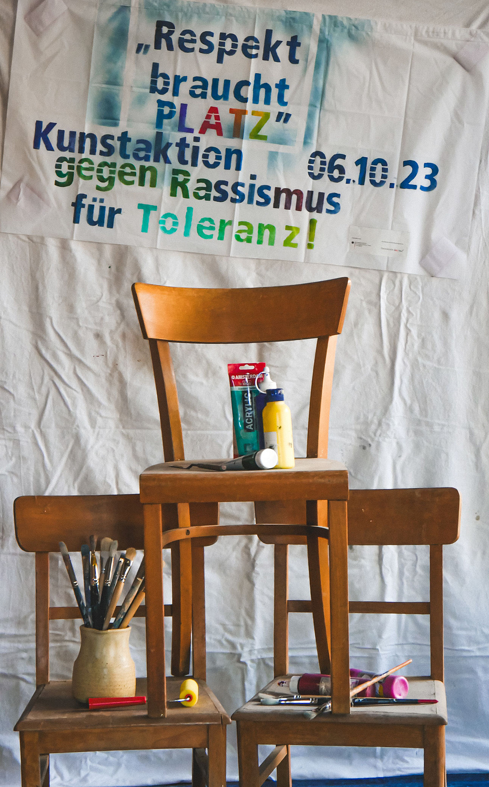 Drei Stühle, dahinter auf Stoff geschrieben: Kunstaktion am 6.10 gegen Rassismus und für toleranz