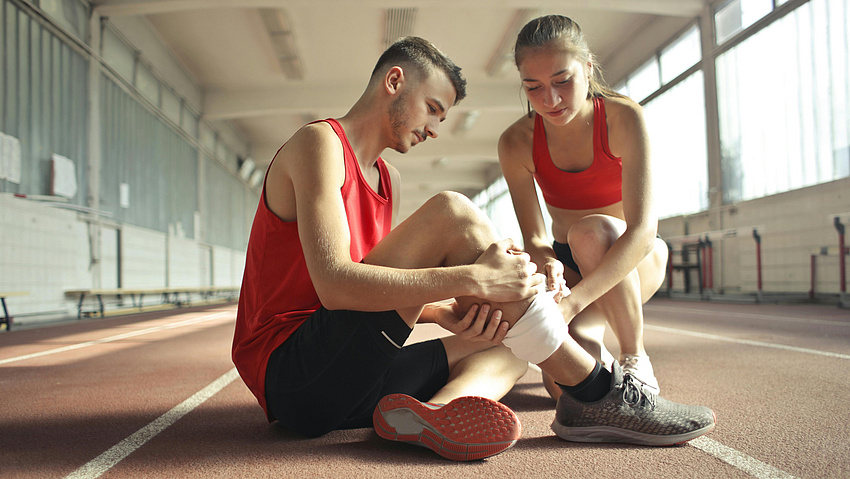 Zwei junge sportlich gekleidete Menschen behandeln eine Verletzung sitzend auf einer Laufbahn