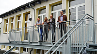 Vier Personen auf einer Metalltreppe vor einem Schulgebäude.