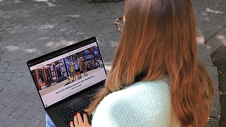Eine Frau sitzt im Freien und arbeitet mit einem Laptop.