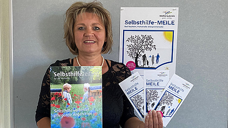 Eine Frau zeigt eine Zeitung und Flyer.