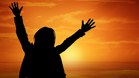 Ein Schatten einer Person mit erhobenen Händen vor einem Sonnenuntergang