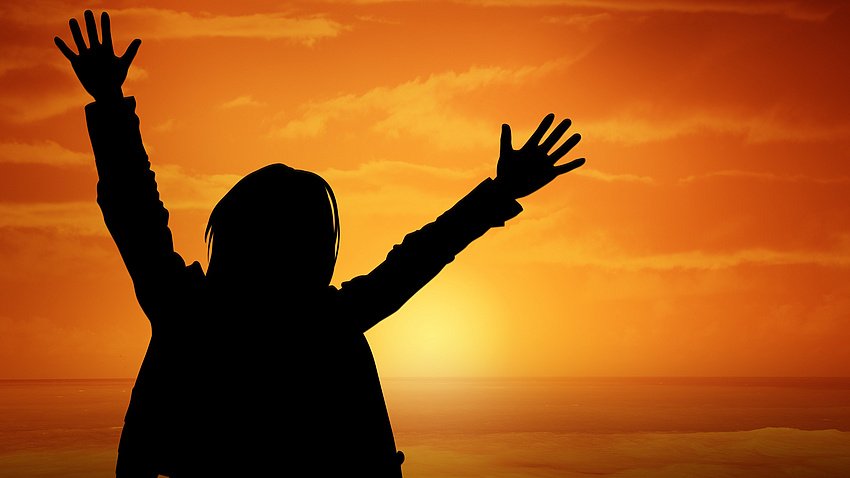 Ein Schatten einer Person mit erhobenen Händen vor einem Sonnenuntergang
