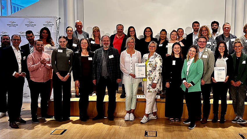 Eine große Gruppe von Leuten lächelt in die Kamera, Sie halten Urkunden in den Händen.