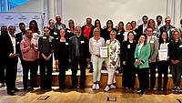 Eine große Gruppe von Leuten lächelt in die Kamera, Sie halten Urkunden in den Händen.