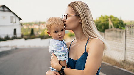 Frau küsst ein Baby, das sie auf dem Arm hält.