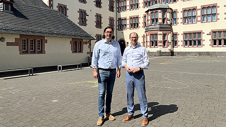 Zwei Männer stehen auf einem Hof vor der Fassade eines historischen Gebäudes.