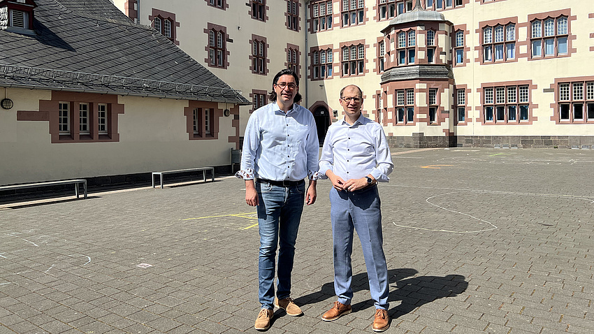 Zwei Männer stehen auf einem Hof vor der Fassade eines historischen Gebäudes.