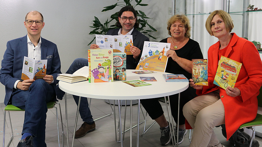 Landrat Jan Weckler, Bürgermeister Kjetil Dahlhaus, Sabine Coldehoff und Stephanie Roser sitzen an einem Tisch und präsentieren Plakate und Bücher.