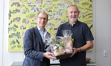 Zwei Männer halten gemeinsamen einen Geschenkkorb, in dem sich einige Lebensmittel befinden.