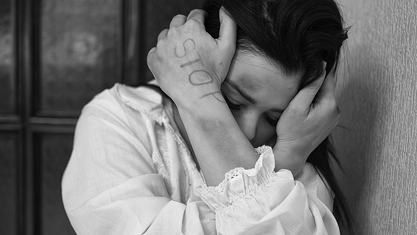 Eine Frau hält sich schützend die Hände vor das Gesicht. An ihrem Körper sind blaue Flecken zu sehen, auf ihrem Handrücken steht in Großbuchstaben geschrieben: STOP.