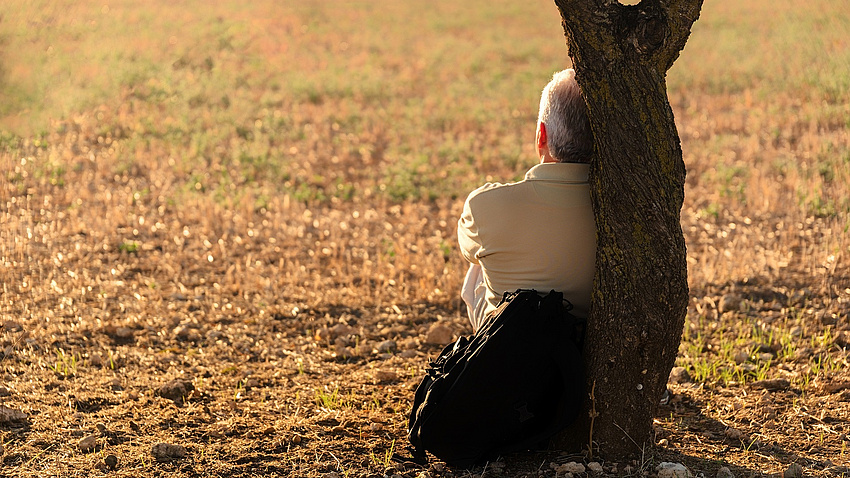 Ein Mann sitzt grübelnd an einen Baum gelehnt.