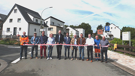 Eine Gruppe von Menschen steht auf einer Straße und durchschneidet ein rot-weißes Band.