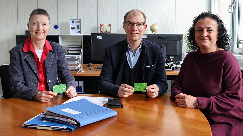 Kreisbeigeordnete Marion Götz, Landrat Jan Weckler und Fachdienstleiterin Nazan Isfen. Sie halten kleine grüne Debitkarten in der Hand.