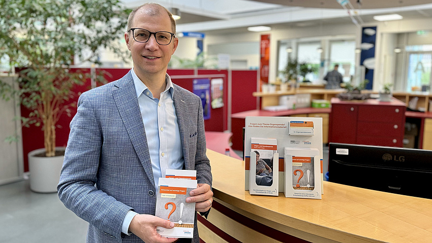 Landrat Jan Weckler steht an einem Tisch. Er hält einen Flyer zum Thema Organspende in die Kamera.