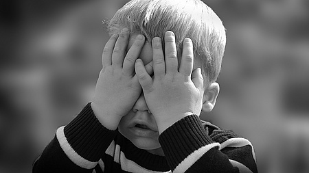 Ein Junge hält sich die Händer vor das Gesicht
